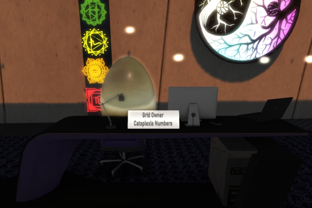 Cataplexia's office desk at AMV Town Hall with a desk lamp, a computer screen and a laptop computer on it as well as a sign which reads, "Grid owner" and "Cataplexia Numbers". A big golden egg is standing upright on the office chair.